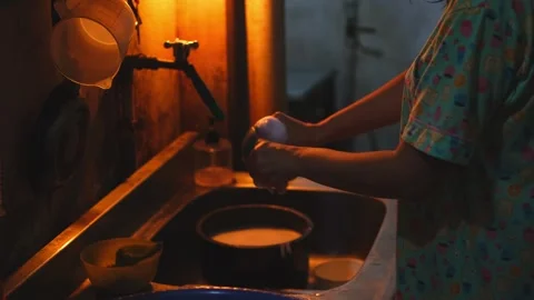 Woman washing dishes in a rustic kitchen sink at night Vídeo Stock 339823853
