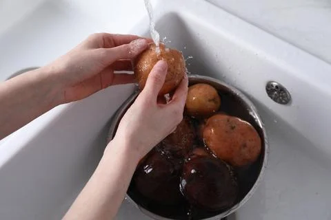 Woman washing fresh potato in kitchen sink, closeup. Cooking vinaigrette sala Stock Photos