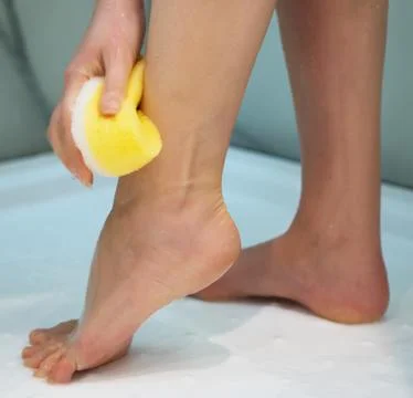 Woman washing her legs with sponge in the shower. Stock Photos