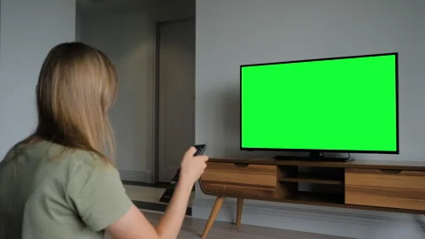 Woman is watching flat smart led TV with blank green screen in grey living room Stock Footage 337057558