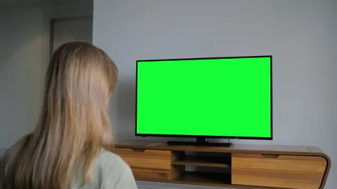 Woman is watching flat smart led TV with blank green screen in grey living room Stock Footage 337058571