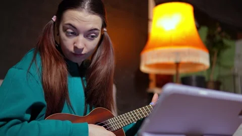Woman is watching tutorial of playing ukulele online and trying to practice it Vídeos de archivo 314290475