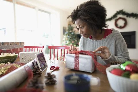 Woman watching video tutorial on digital tablet, wrapping Christmas gift at dini 写真素材