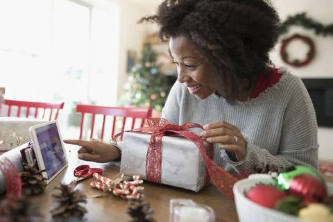 Woman watching video tutorial on digital tablet, wrapping Christmas gift at dini Stock Photos