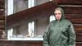 Woman in waterproof raincoat stands near uninhabited house HD Footage