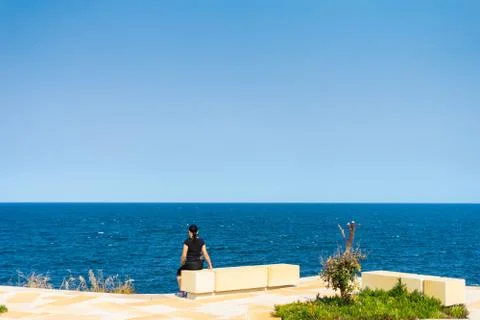 Woman wearing active wear sitting on sandstone block facing view of the ocean Stock Photos