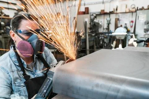 Woman wearing safety glasses and dust mask standing in metal workshop Stock Photos