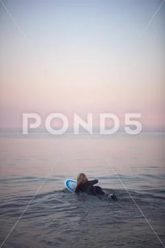 Woman Wearing Wetsuit Paddling Floating Surfboard Out Onto Calm Sea Stock Photos