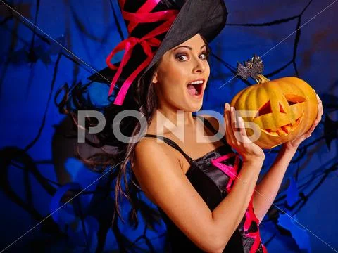 Woman wearing witch hat keeps big orange pumpkin. Stock Photos