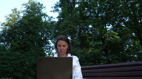 Woman in white jacket types on computer in green park Stock Footage 167500037