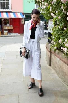 Woman in white linen suit using phone in street, full length Stock Photos
