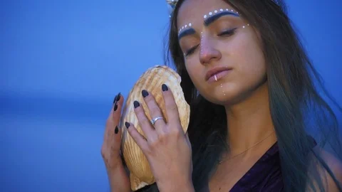 A woman with white patterns on her face examines a large seashell Stock Footage 81325285