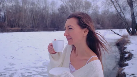 Woman in a white pullover drinks hot drink from a white cup on the bank of the i Stock Footage 169636962