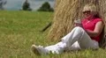 Woman with white smartphone sits near haystack and listens to music HD Footage