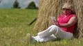 Woman with white smartphone sitting near haystack and listening to music HD Footage