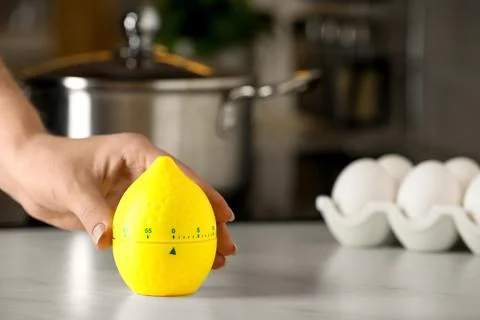 Woman winding up kitchen timer in shape of lemon at table indoors Stock-Fotos