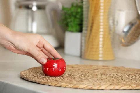 Woman winding up kitchen timer in shape of tomato at white table indoors, clo Stock Photos