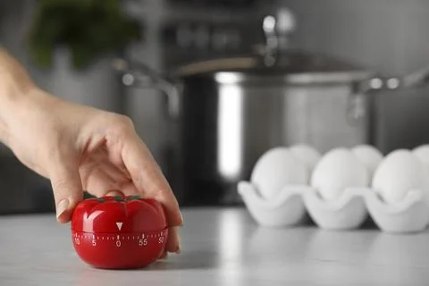 Woman winding up kitchen timer in shape of tomato at white table indoors, c.. Foto stock