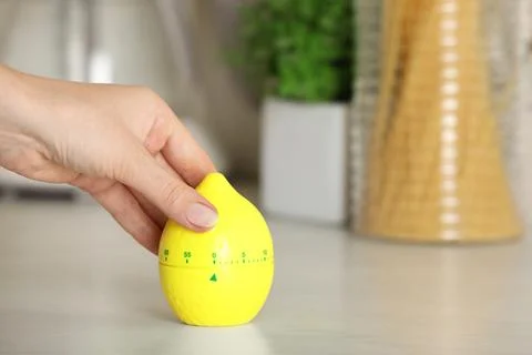 Woman winding up kitchen timer in shape of lemon at white table indoors, cl.. Stock Photos
