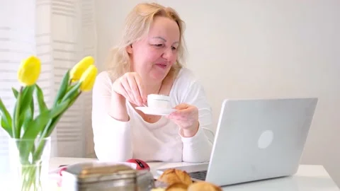 Woman at window drinking tea coffee near computer chatting with friends spending Stock Footage 238476913