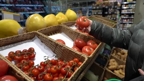 Woman in winter down jacket choosing ripe large tomatoes in store Stock Footage 304774325