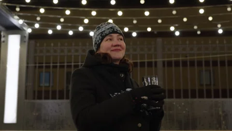 Woman in winter hat looking up at string lights on terrace at night Stock Footage 319120996