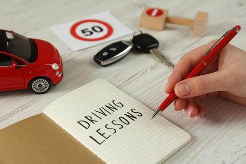Woman with workbook for driving lessons at white wooden table, closeup. Passi Stock Photos