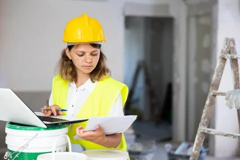 Woman worker checking documents and using laptop in construction site Foto stock