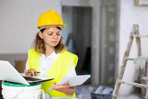 Woman worker checking documents and using laptop in construction site 写真素材