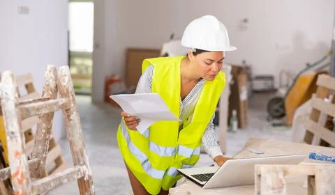Woman worker checking documents and using laptop in construction site Stock Photos