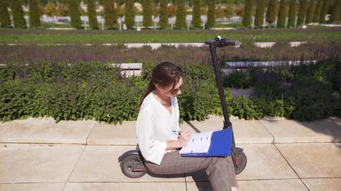 Woman worker develops technology in a notebook, sitting on an electric scooter Stock Footage 116557926