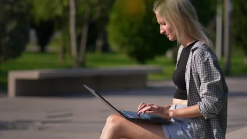 Woman working and using laptop computer outdoors in park, sitting on bench, 스톡 동영상 250625804