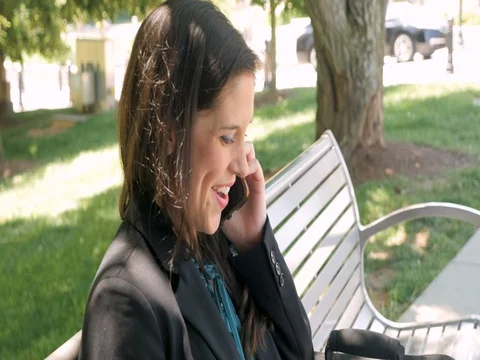 Woman working on a computer on a park bench answering her smart phone Stock Footage 78510393
