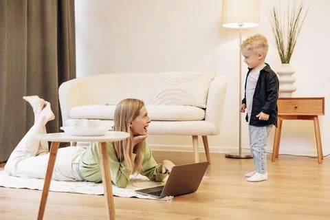 Woman working on computer while her son playing around Stock Photos
