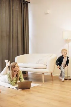 Woman working on computer while her son playing around Stock Photos