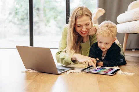 Woman working on computer while her son playing on tablet games Stock Photos