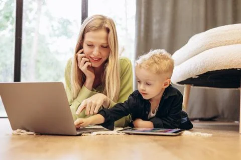 Woman working on computer while her son playing on tablet games Stock Photos
