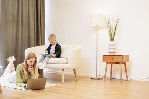 Woman working on computer while her son playing on tablet games Stock Photos