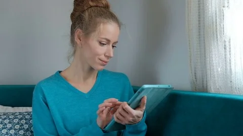 A woman is working happily on a tablet while sitting on the couch Video stock 74322176