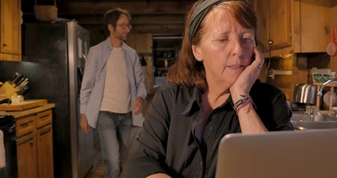 Woman working on her computer while a man is cooking and cleaning behind her Stock Footage 128590536