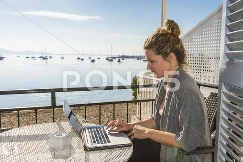 Woman Working On Her Laptop On A Balcony Overlooking The Ocean, Port De