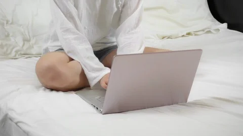 Woman working with her laptop while sitting on a snow-white bed, top view Video stock 123945724