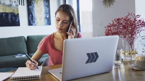 Woman working from home doing notes and talking on the phone Video stock 137957365