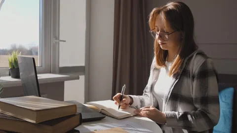 Woman working from home taking notes and reading a book Stock Footage 314525611