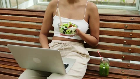 Woman working on a laptop computer and eating healthy salad outdoors Stock Footage 340554287