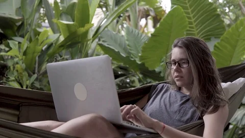Woman working on laptop while sitting on hammock, exotic background Video stock 84842891