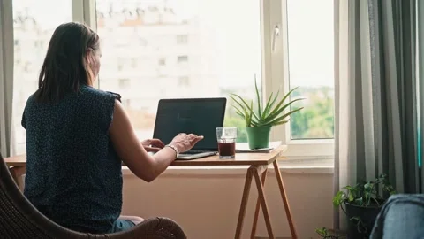 A woman working on a laptop while sitting at the table opposite a window Stock Footage 200730916