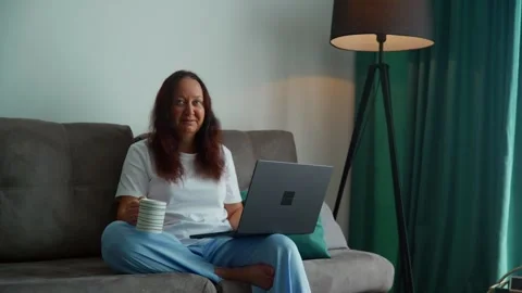 Woman working on laptop while sitting on couch in modern apartment 库存影片 339631966