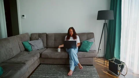 Woman working on laptop while sitting on sofa in modern apartment Stock Footage 339632014