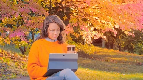 Woman working with notebook, drinking coffee, enjoying autumn in park Stock Footage 112601871